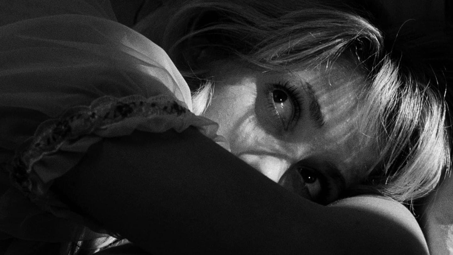 Close no rosto parcialmente coberto de Catherine Deneuve, em preto e branco.