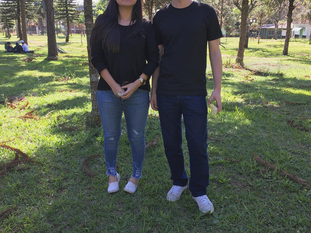 Homem e mulher, lado a lado em um gramado, com roupas parecidas — camisetas pretas, calças jeans e tênis branco.